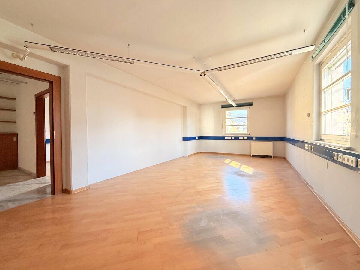 Langes, helles Büro mit Holzfußboden und einem Fenster, das viel Tageslicht hereinlässt, in gutem Zustand.