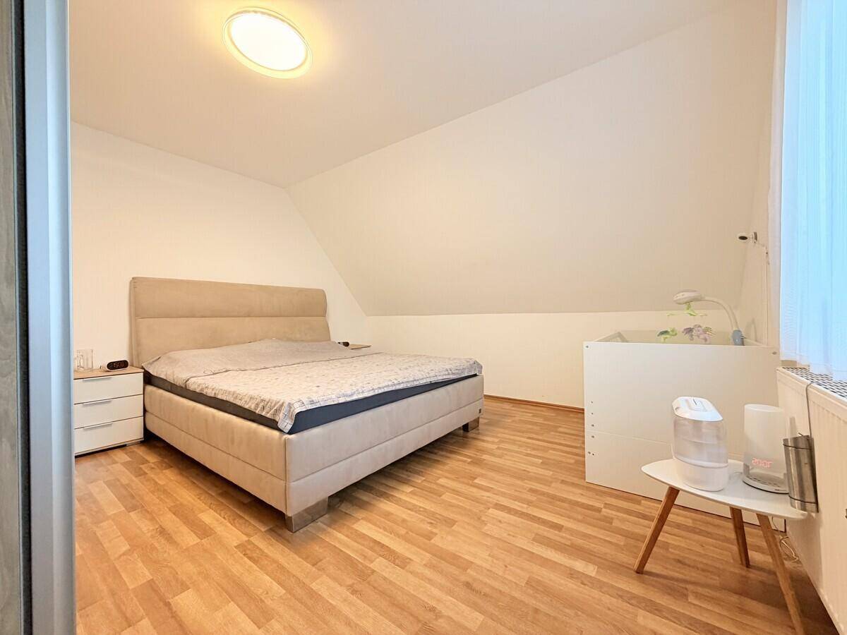Geräumiges Schlafzimmer mit Doppelbett, Babybett, Laminatboden und Dachschräge.