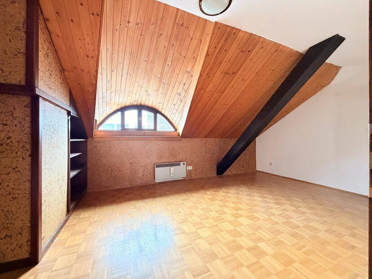 Ausgebautes Dachgeschoss mit Holzverkleidung, Parkettboden und einem charmanten Rundbogenfenster.
