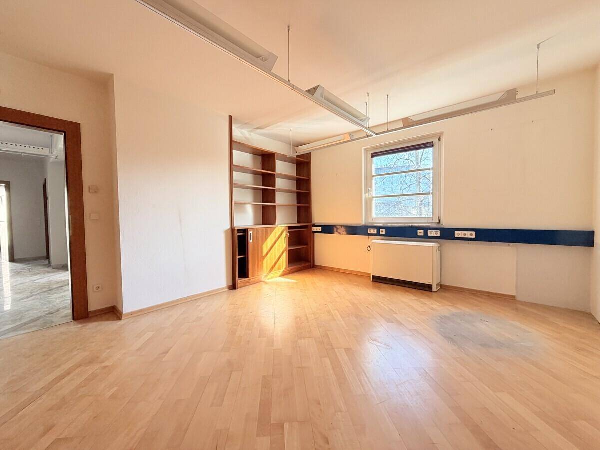 Heller Büroraum mit Holzfußboden, Einbauregalen und einem Fenster, das viel Tageslicht hereinlässt.