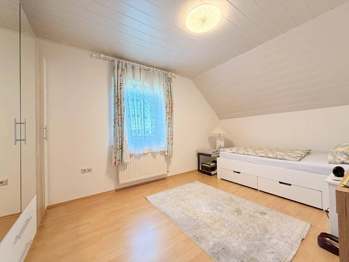 Gemütliches Schlafzimmer im Dachgeschoss mit Holzboden und Fenster.