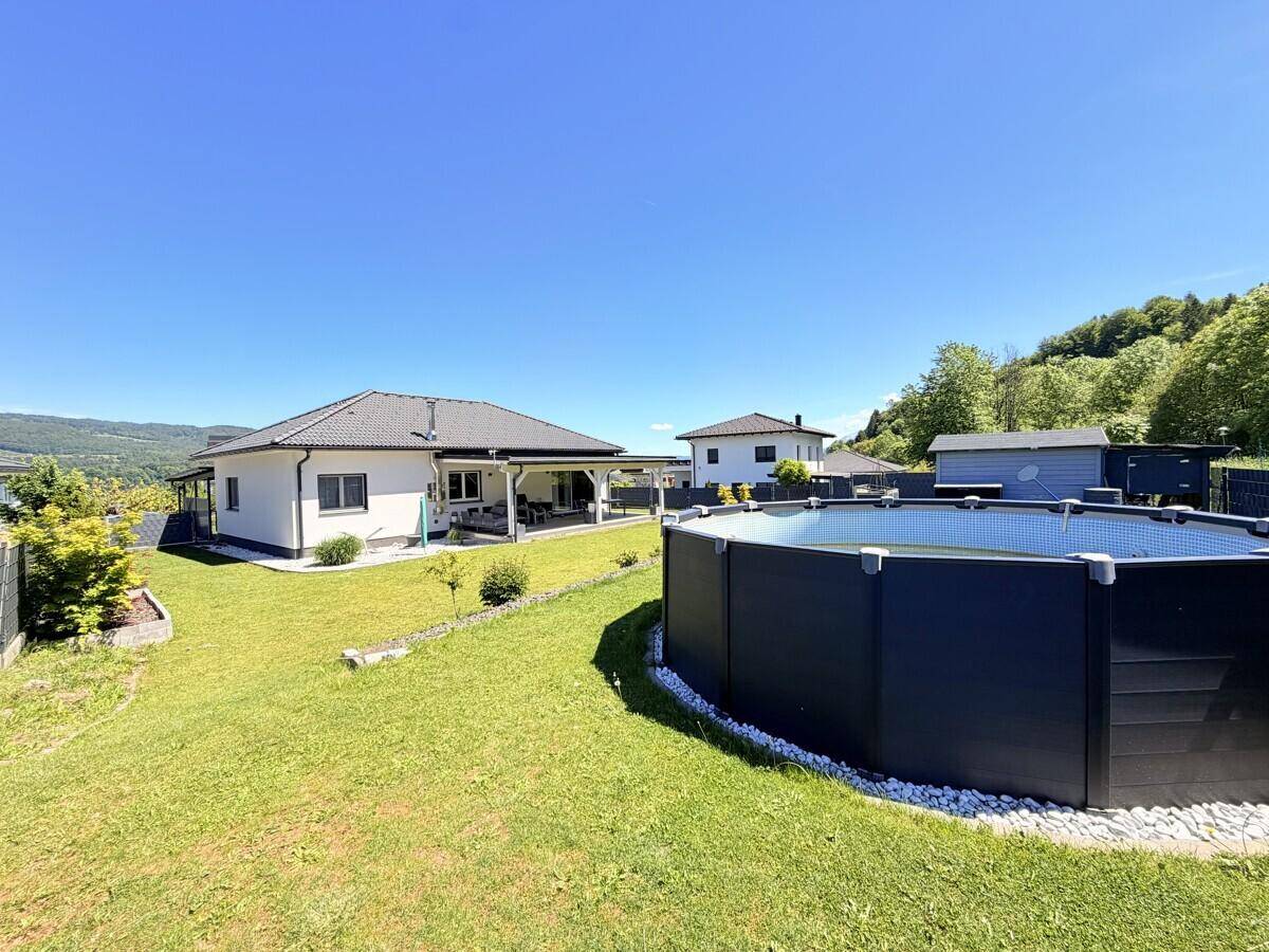 Sonniger Gartenbereich mit großem Aufstellpool, Rasenfläche und Blick auf die umliegende Landschaft.