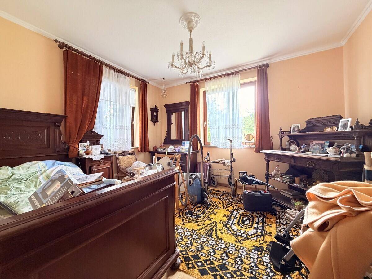 Schlafzimmer mit traditionellen Holzmöbeln, Teppich und zwei Fenstern für viel Tageslicht.
