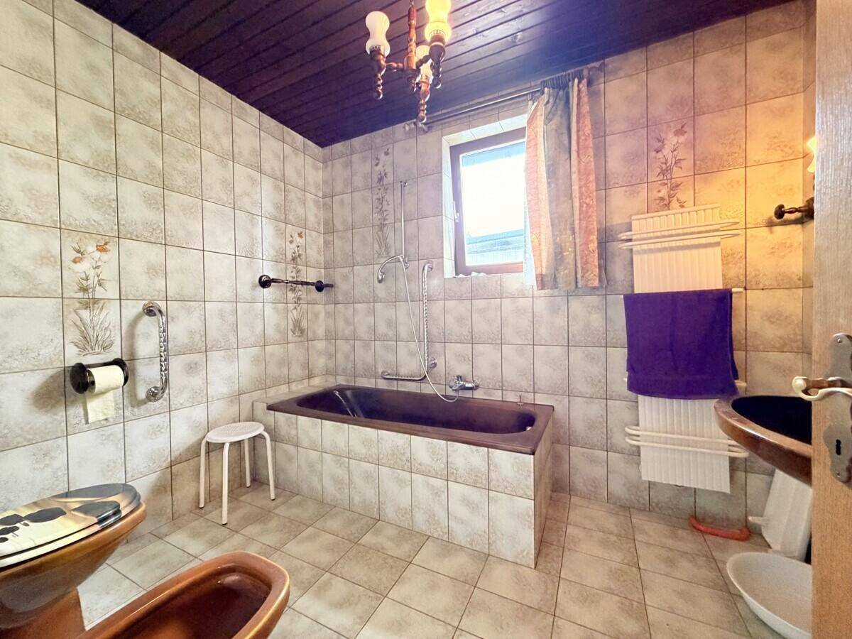 Badezimmer im 80er-Jahre-Stil mit Fliesen, Badewanne, WC und Fenster für natürliche Belüftung.