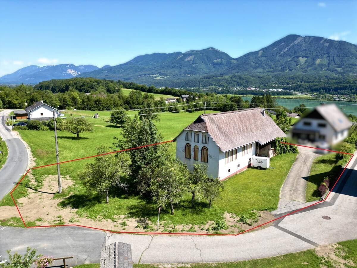 Luftaufnahme des Grundstücks mit roter Umrandung, See- und Bergblick.