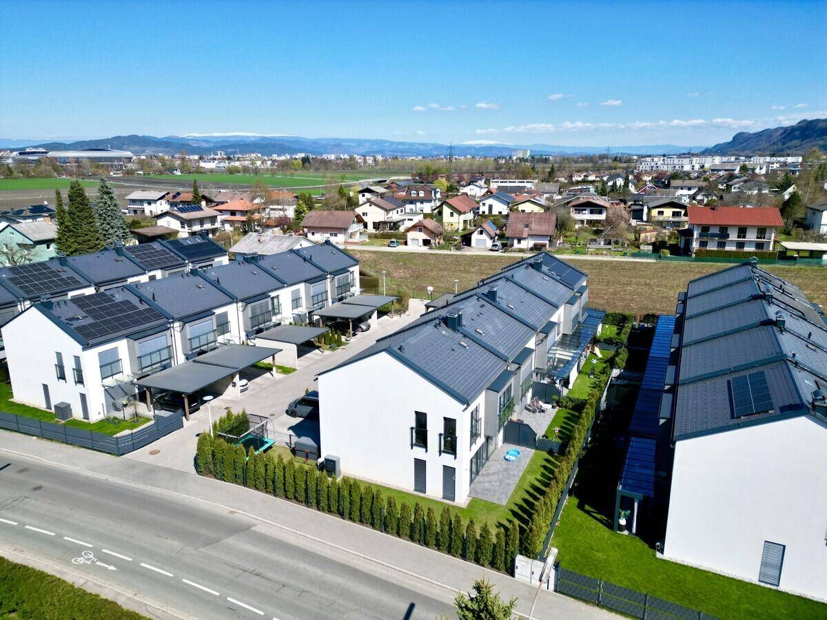Luftaufnahme einer modernen Wohnsiedlung mit Reihenhäusern, Gärten und umliegender Landschaft.
