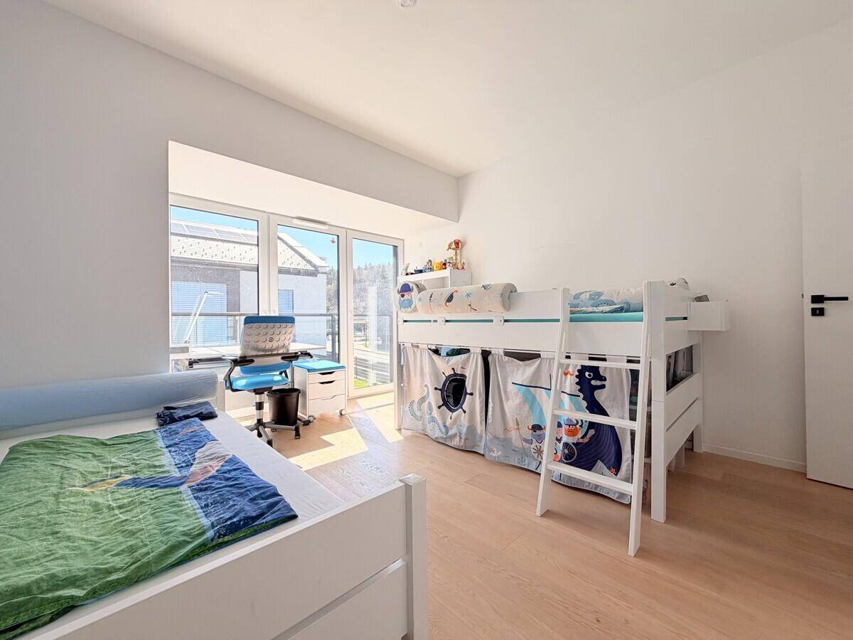 Helles Kinderzimmer mit Etagenbett, Schreibtisch und großen Fenstern für viel Tageslicht.