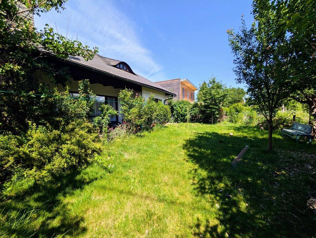 Großer, grüner Garten mit Rasenfläche und Bäumen neben dem Haus unter strahlend blauem Himmel.