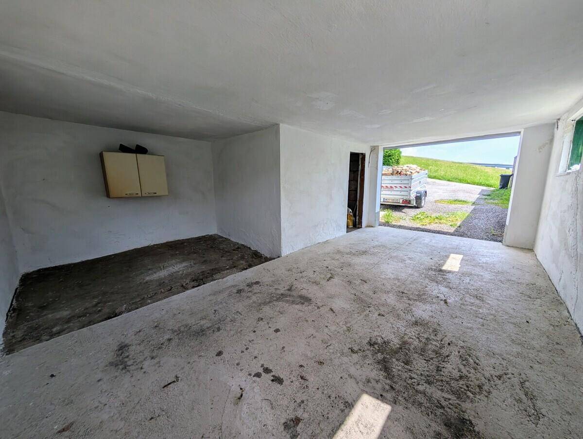 Leere Garage mit Betonboden und offenem Tor, bietet vielseitige Nutzungsmöglichkeiten.