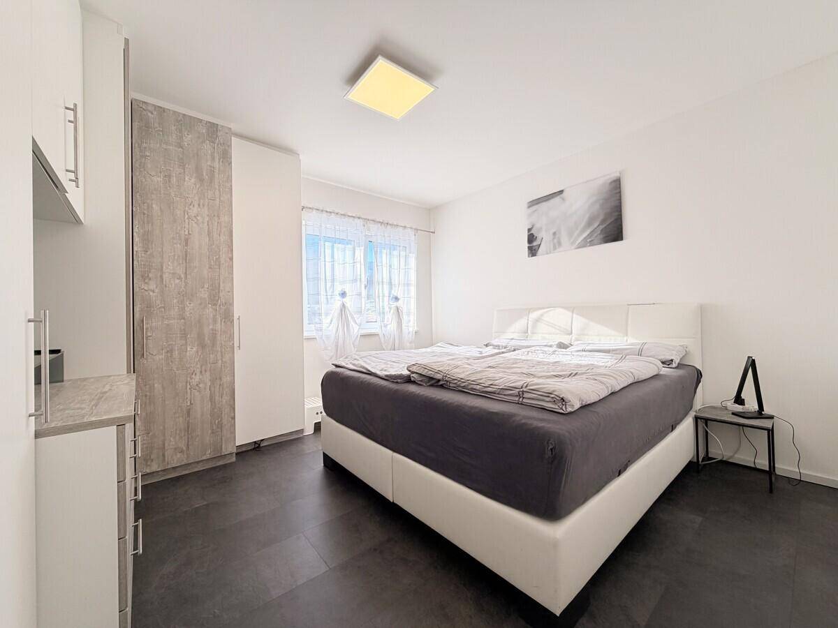 Helles Schlafzimmer mit modernem Doppelbett, dunklem Boden und weißem Kleiderschrank.