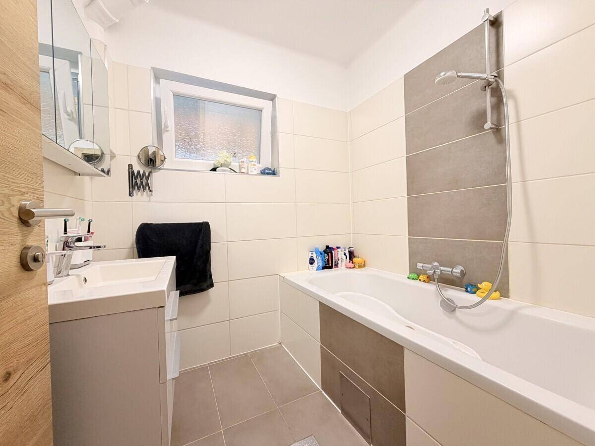 Badezimmer mit Badewanne, Einzelwaschbecken, Spiegelschrank und Fenster.