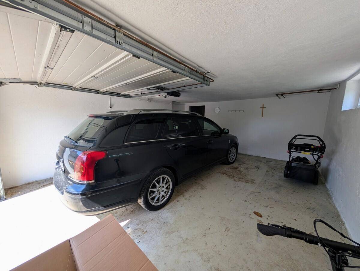 Geräumige Garage mit Betonboden und einem geparkten Auto, bietet Platz für Fahrzeuge.