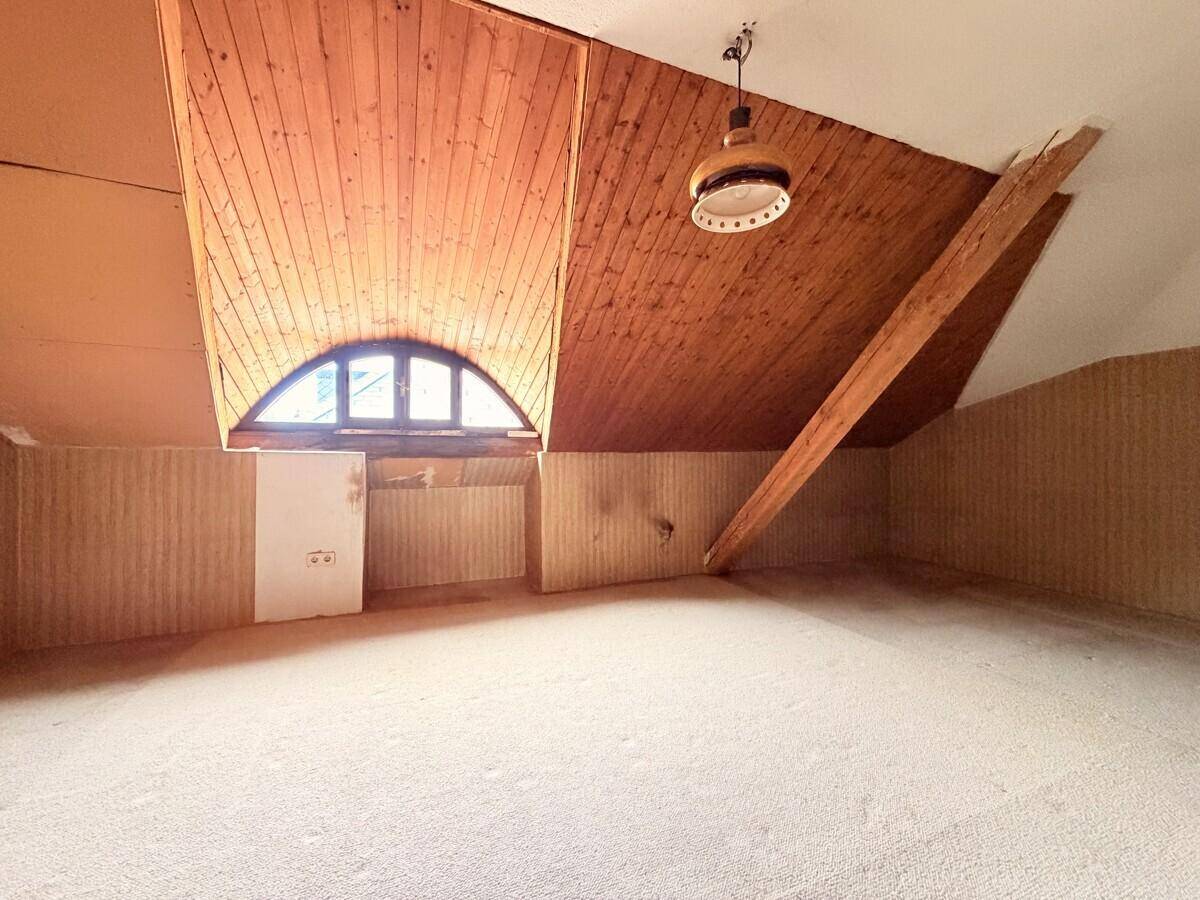Geräumiges Dachgeschoss mit Holzverkleidung, Teppichboden und einem dekorativen Rundbogenfenster.