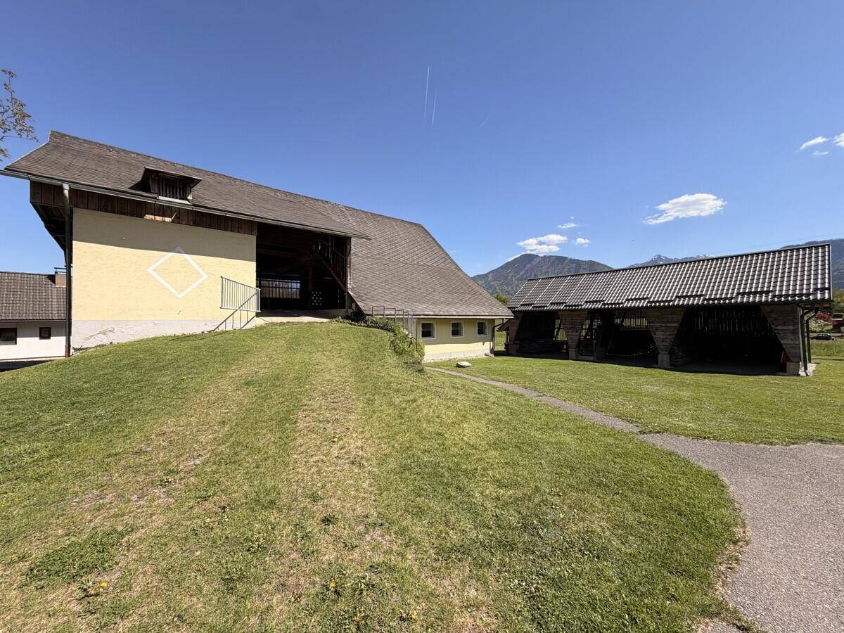 Historisches Bauernhaus auf einem Hügel mit weitläufiger Rasenfläche und einem weiteren Nebengebäude im Hintergrund.