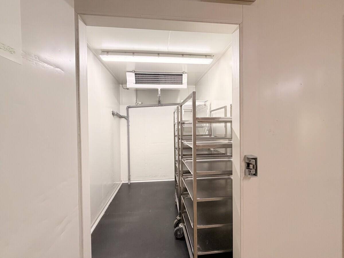 Innenansicht eines Kühlraums mit Metallregalen und einer Kühlanlage an der Decke, bereit für die Lagerung.