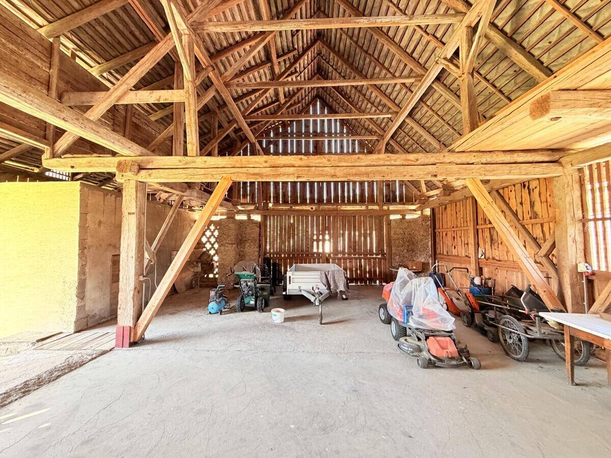 Großer offener Holzschuppen mit robusten Holzbalken und verschiedenen Gartengeräten auf dem Betonboden.