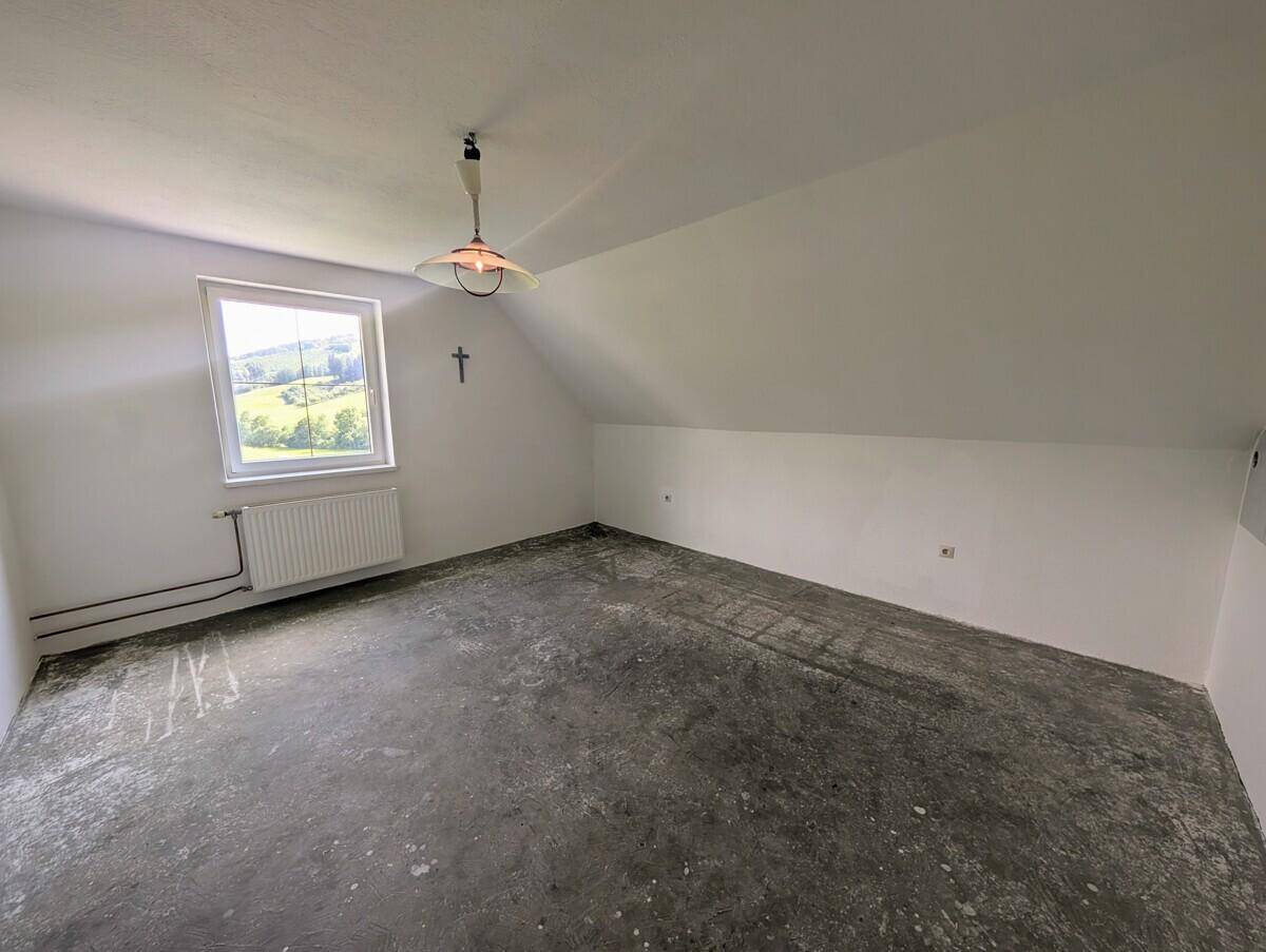 Unfertiger Raum im Dachgeschoss mit Betonboden und Fenster, ideal für Ausbauprojekte.