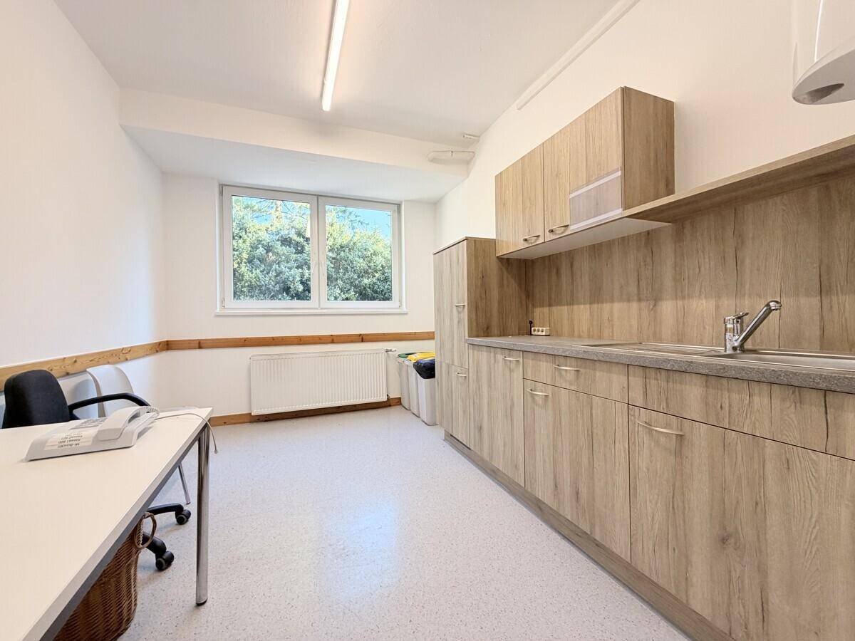 Helles Büro mit kleiner Küchenzeile, Fenster und Schreibtisch, ideal für Mitarbeiter und Pausen.