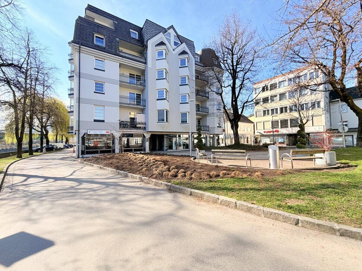Ansicht des modernen Mehrfamilienhauses mit mehreren Balkonen und umliegender Grünfläche unter blauem Himmel.