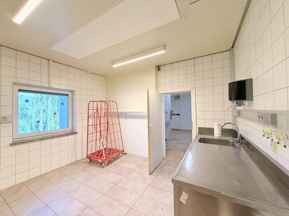 Nutzraum mit gefliesten Wänden, einem Fenster und einer Edelstahlspüle, ideal für Vorbereitungsarbeiten.