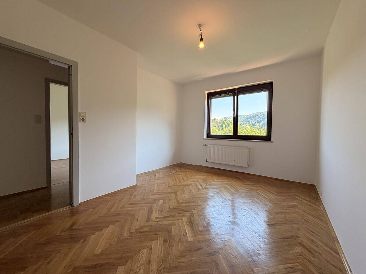 Freundliches Zimmer mit Fischgrätparkett, weißen Wänden und Fenster mit Ausblick.