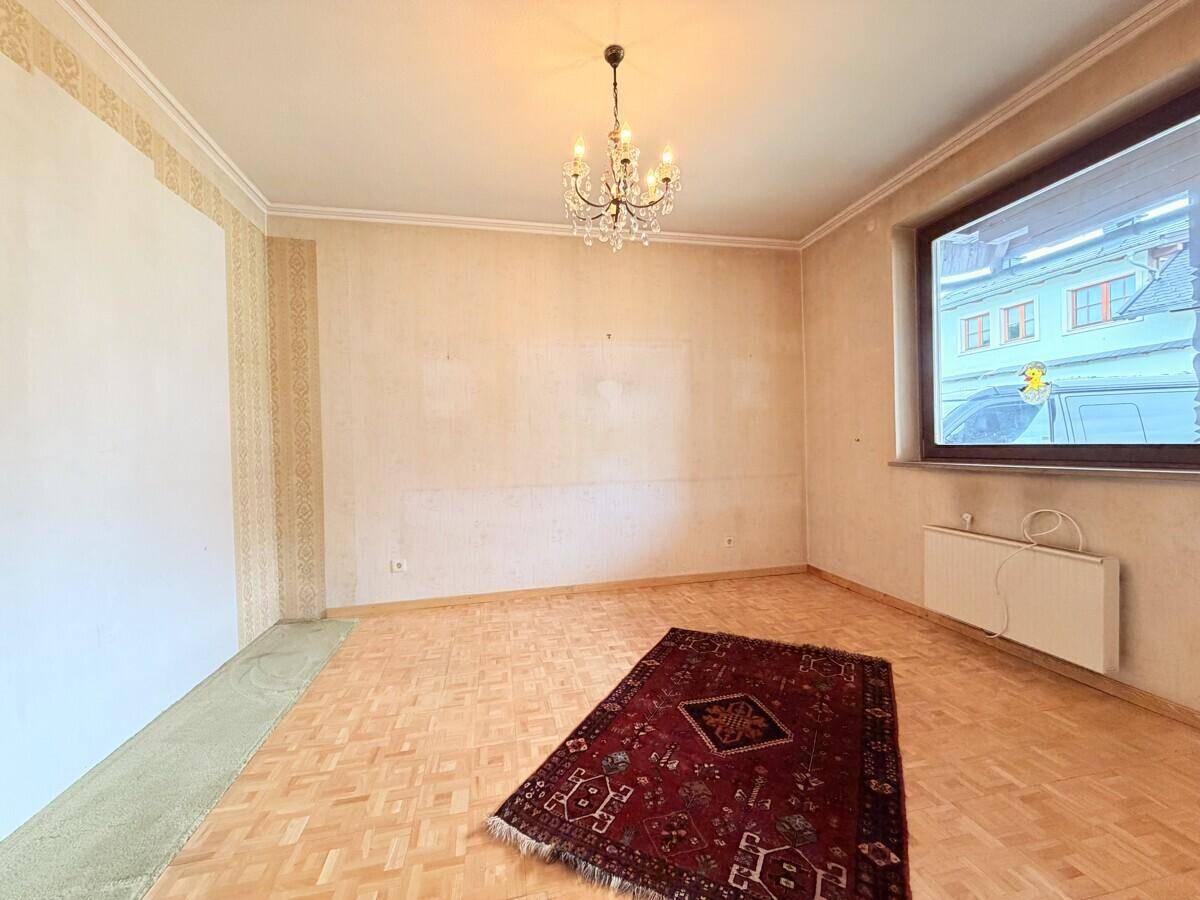 Helles Zimmer mit Parkettboden, einem Fenster und einem Teppich, bereit zur individuellen Gestaltung.