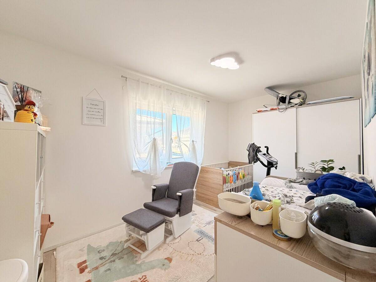 Freundliches Kinderzimmer mit Babybett, Schaukelstuhl und viel natürlichem Licht durch das Fenster.