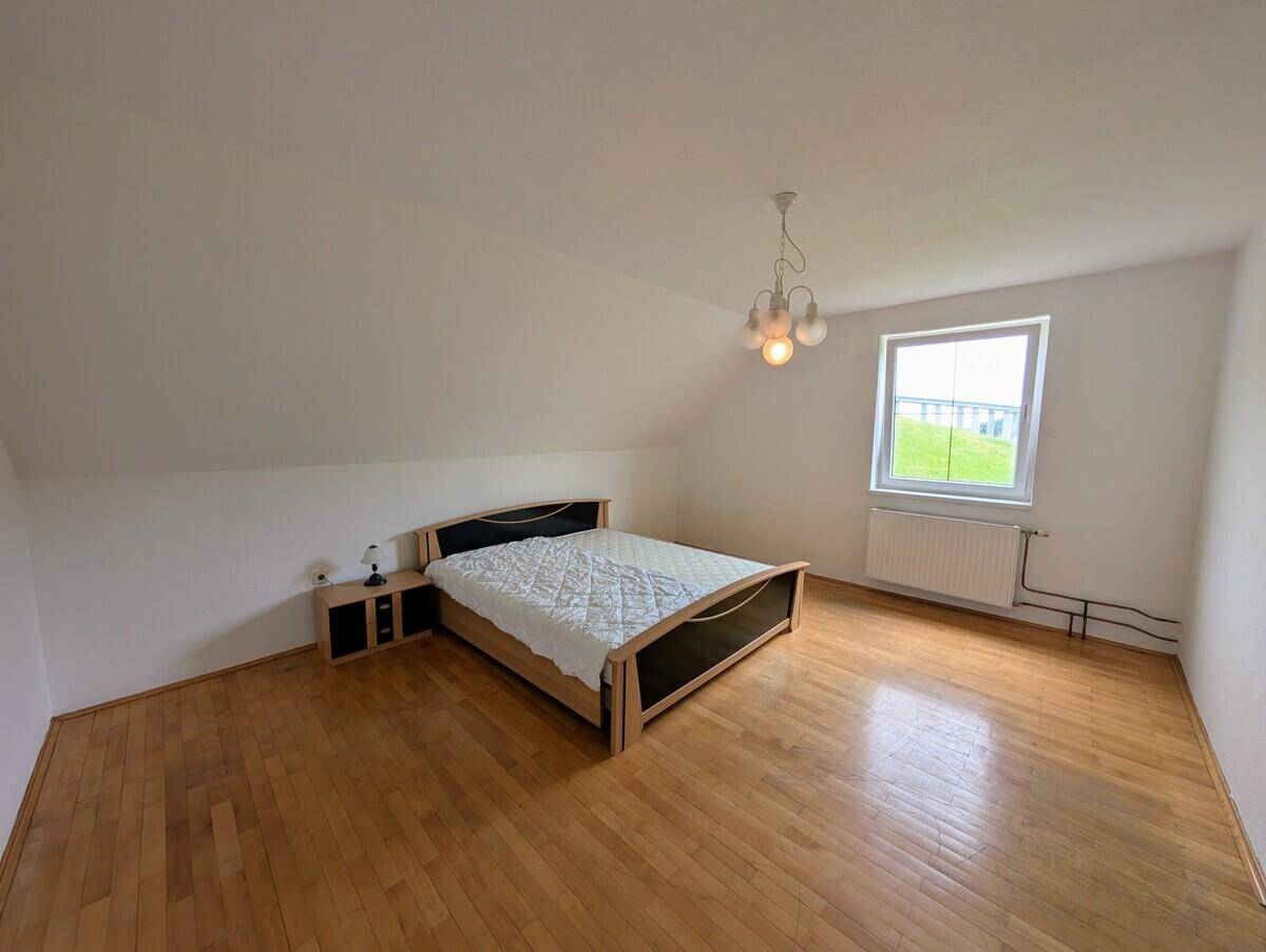Helles Schlafzimmer im Dachgeschoss mit Doppelbett, Nachttischen und schrägen Wänden.
