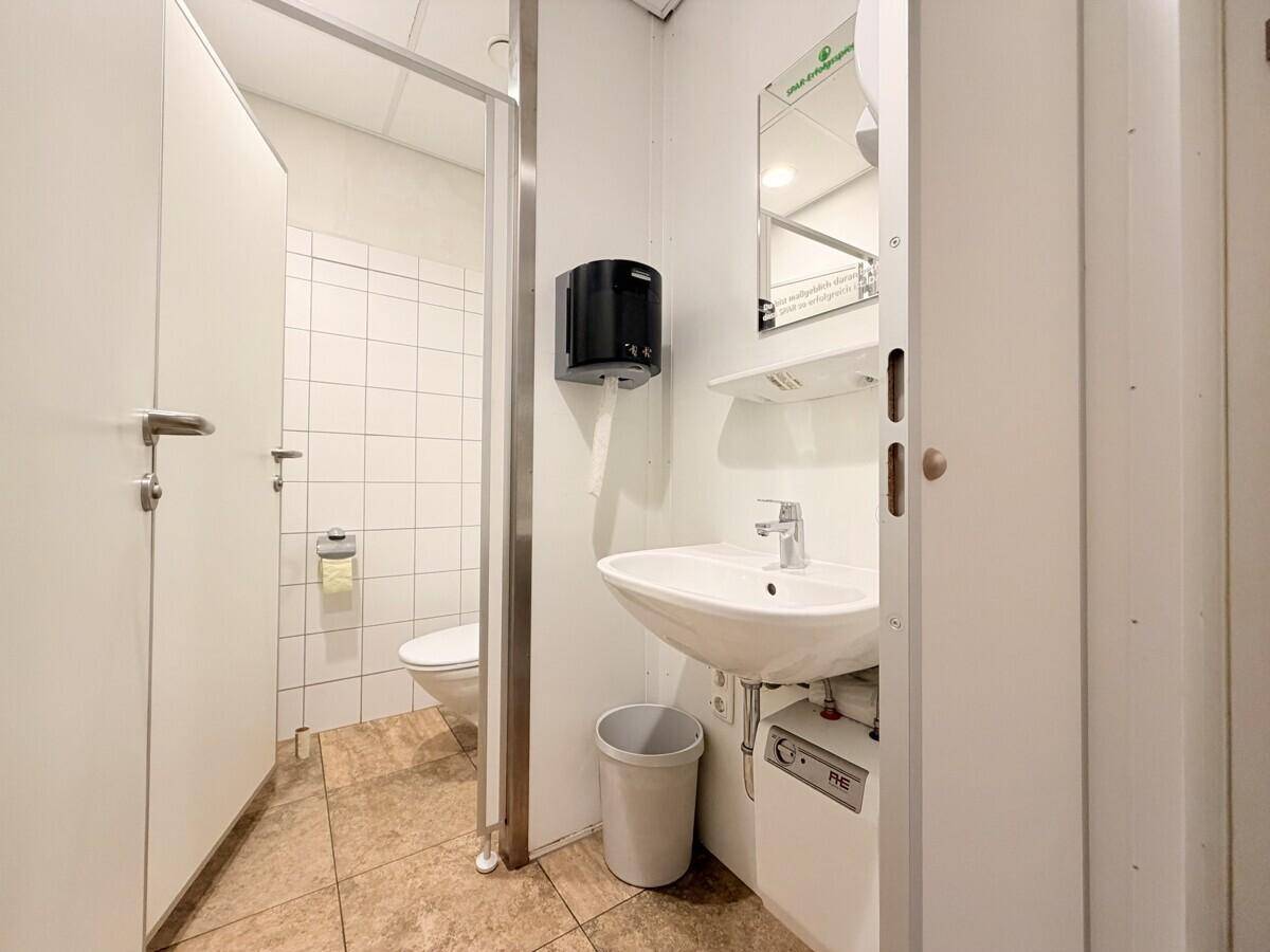 Einfache öffentliche Toilette mit Waschbecken, Spiegel und gefliesten Wänden, funktional und sauber.