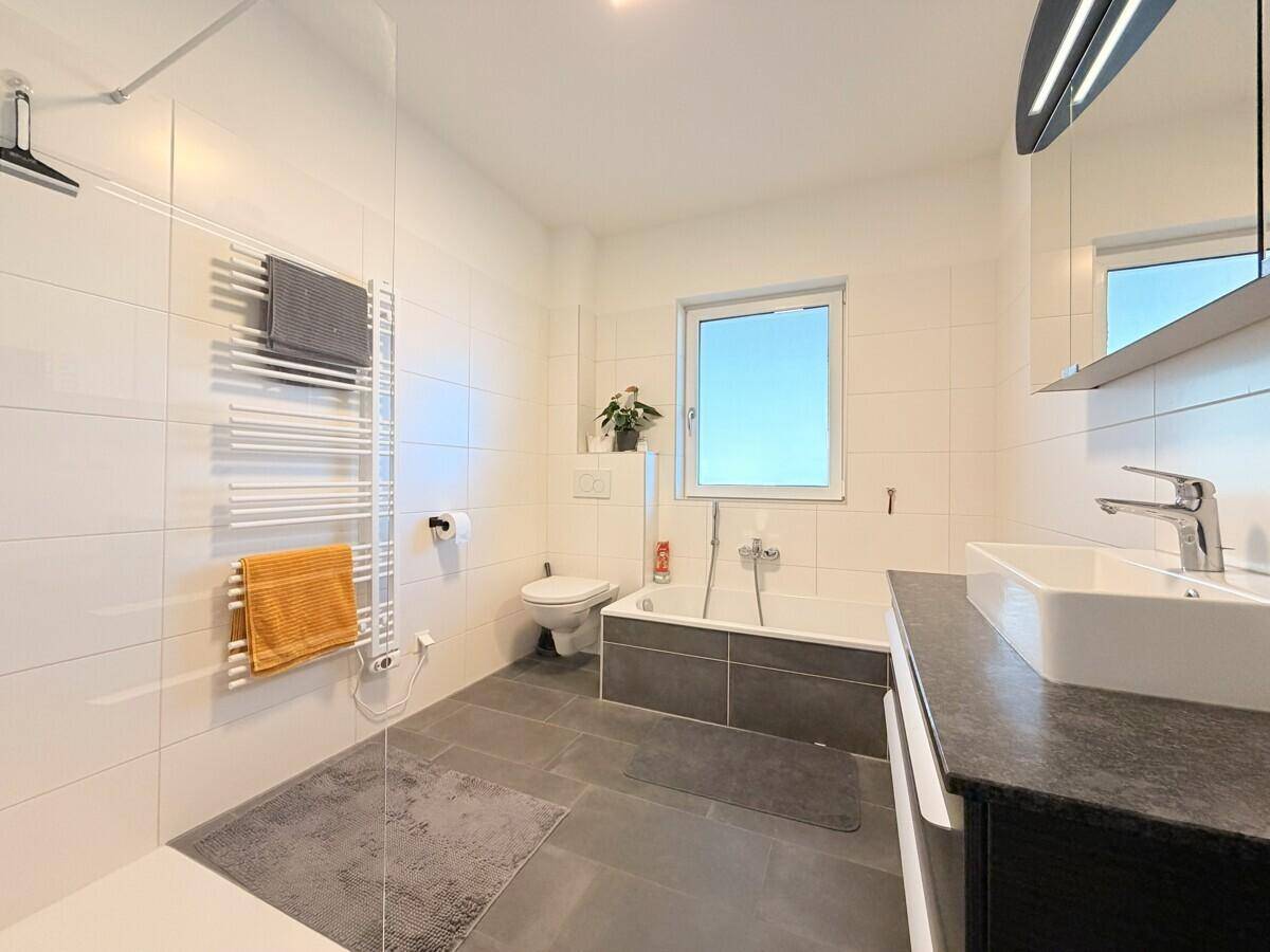 Modernes Badezimmer mit Badewanne, separater Dusche, Einzelwaschbecken und Fenster für Tageslicht.