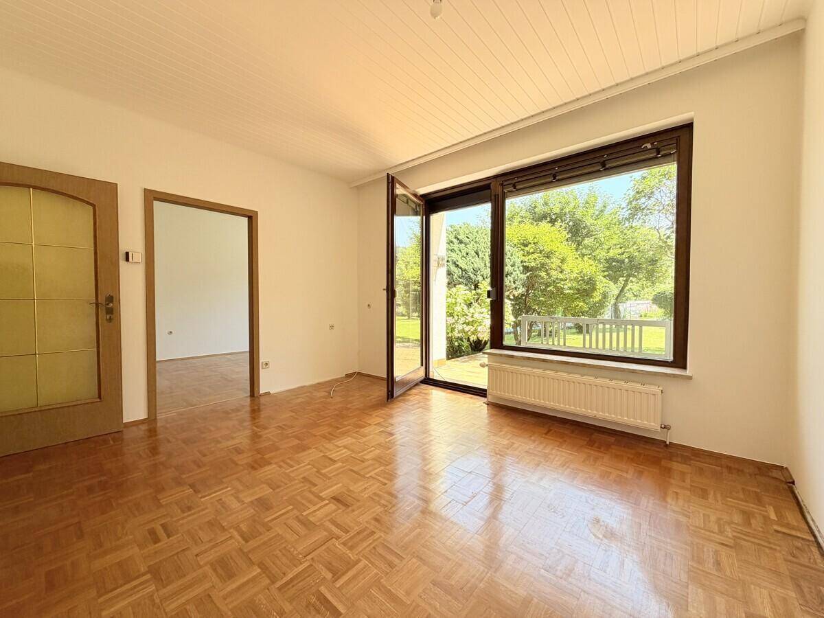 Wohnzimmer mit Parkettboden und großem Fenster, das Zugang zum Garten bietet.