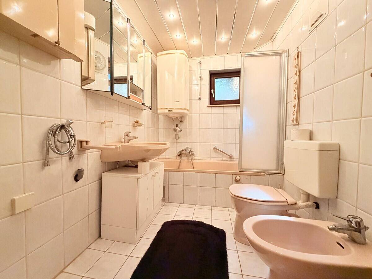 Badezimmer im Stil der 80er Jahre mit beigefarbenen Fliesen, Badewanne und Bidet.