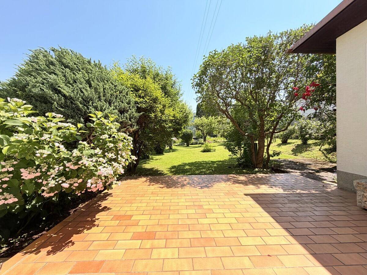 Sonniger Terrassenbereich mit Terrakottafliesen und üppiger Bepflanzung im Garten.