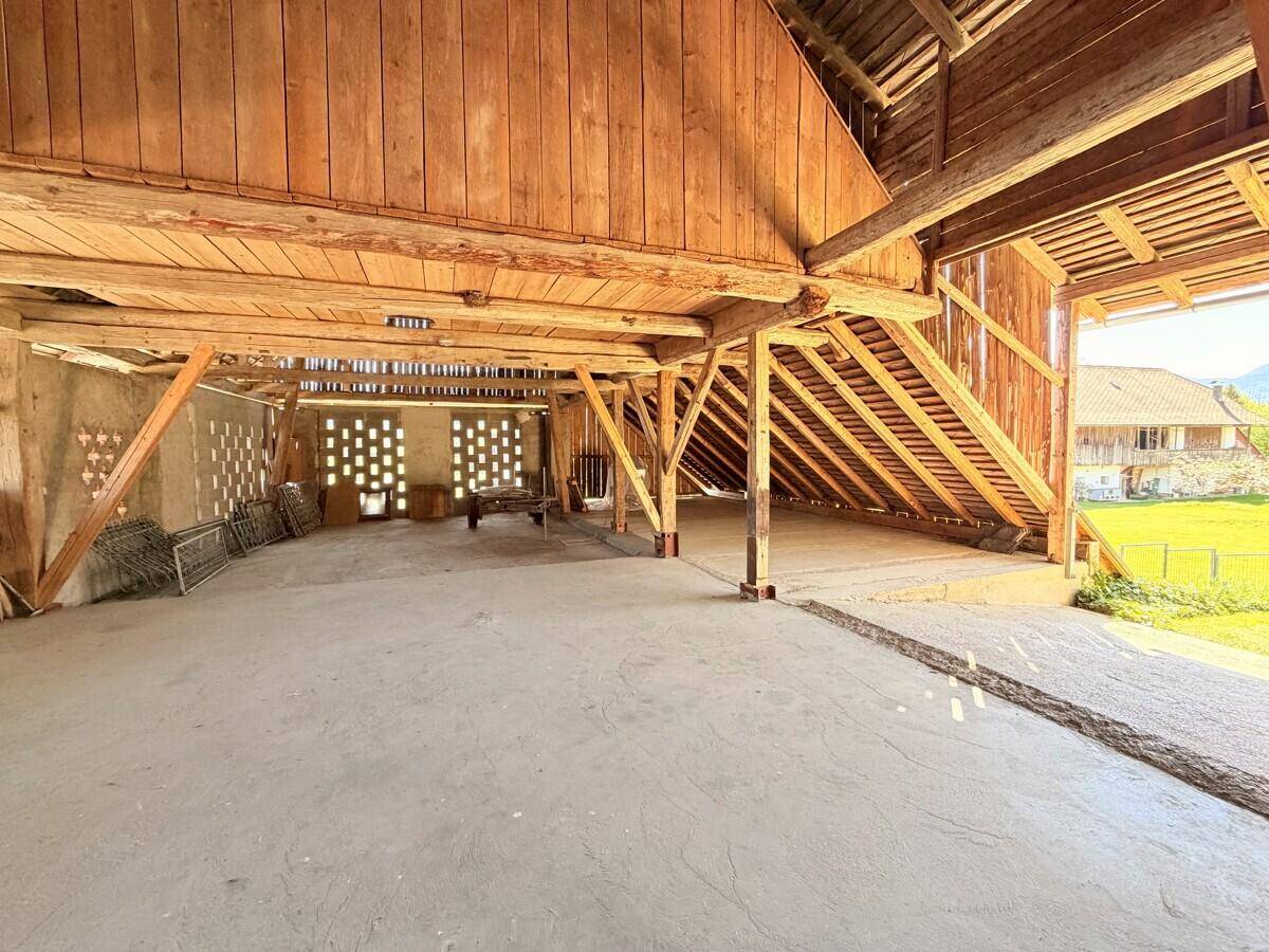 Geräumiger Innenraum eines Holzschuppens mit sichtbaren Holzbalken und einem Betonboden, ideal als Lagerfläche.