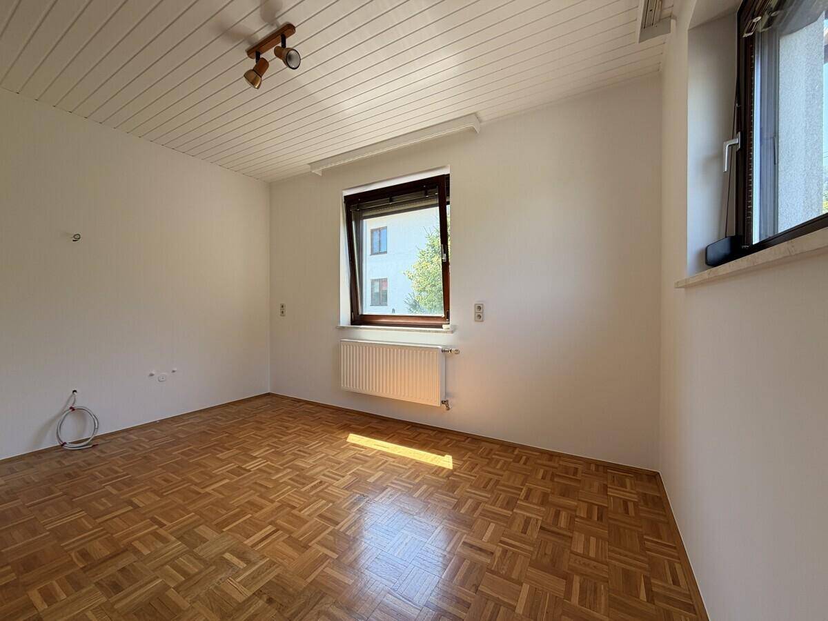 Geräumiges Zimmer mit Parkettboden, weißen Wänden und viel Tageslicht.