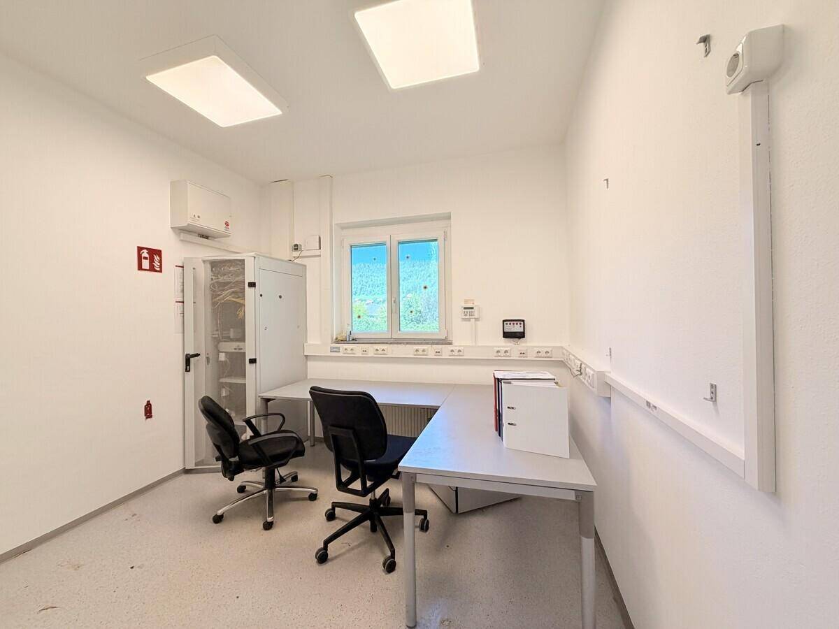 Modernes Büro mit Schreibtischen, Bürostühlen und einem Fenster, das viel Tageslicht hereinlässt.