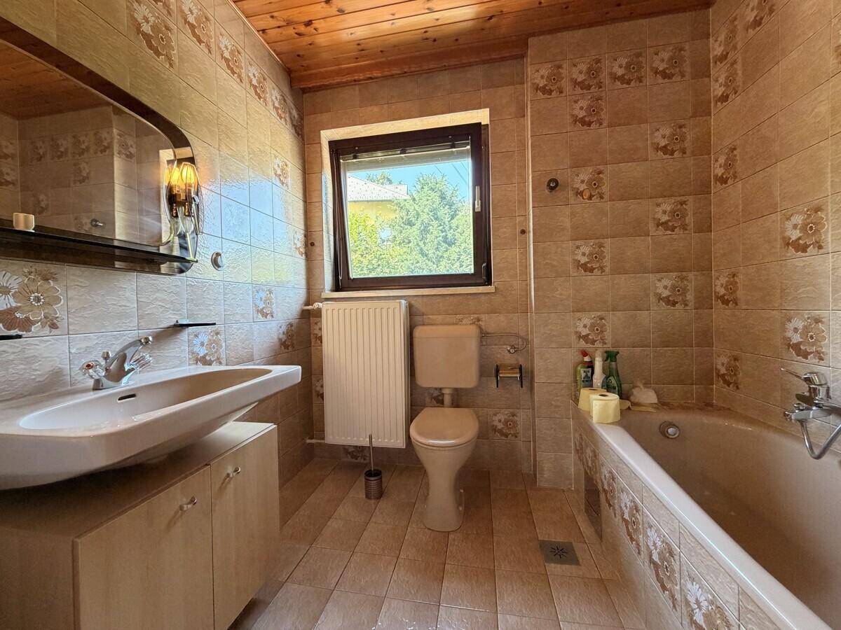 Badezimmer im 80er-Jahre-Stil mit Badewanne, WC, Waschbecken und Holzdecke.