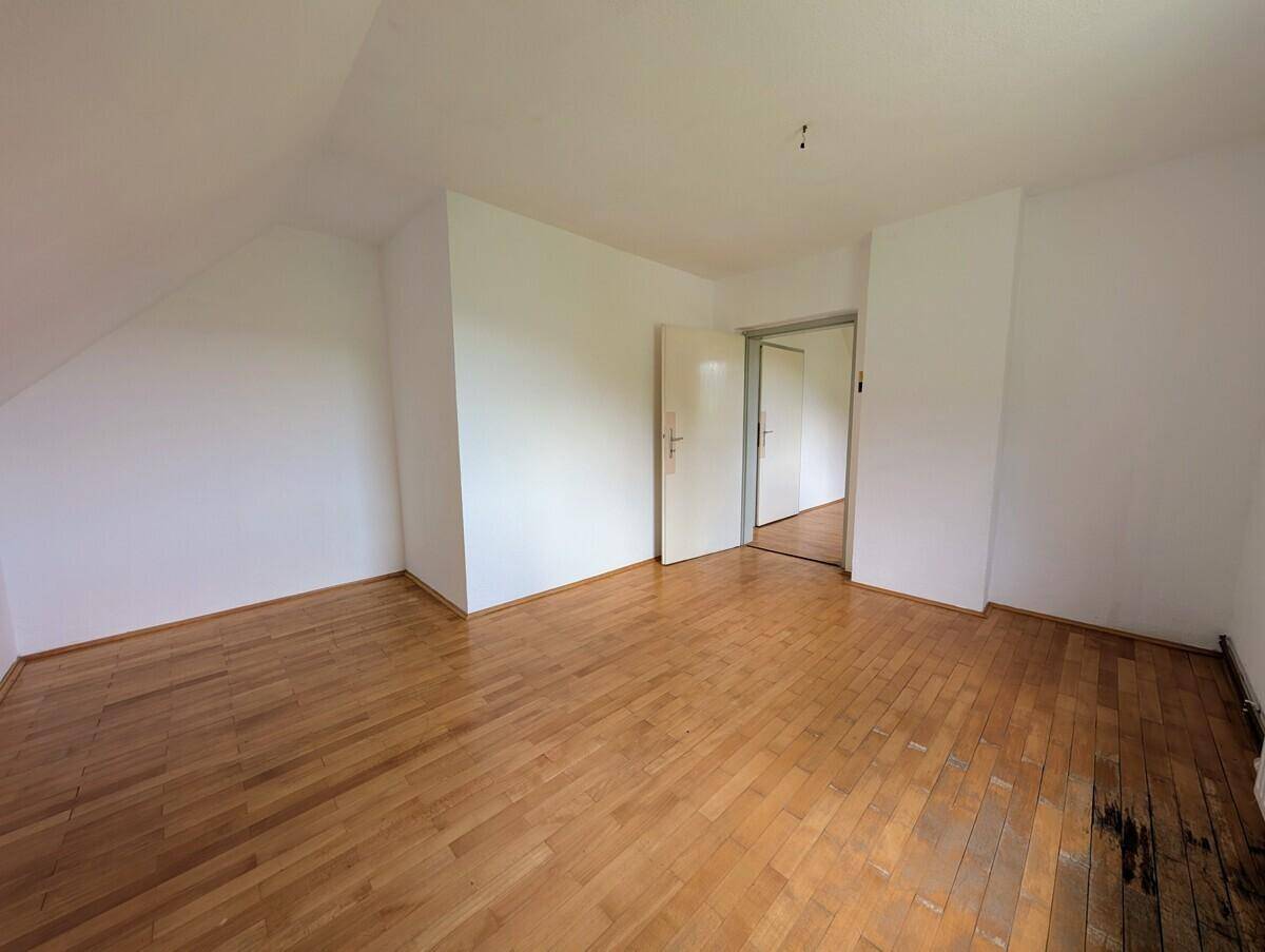 Leeres Zimmer mit Holzparkett und schrägen Wänden, bereit zur individuellen Gestaltung.