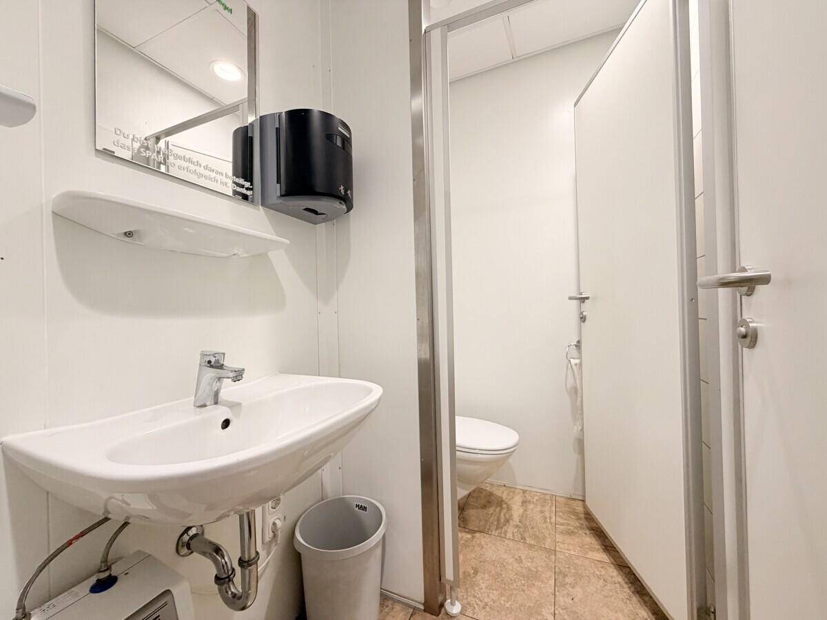 Saubere öffentliche Toilette mit Waschbecken, Spiegel und gefliesten Wänden, funktional und hell.
