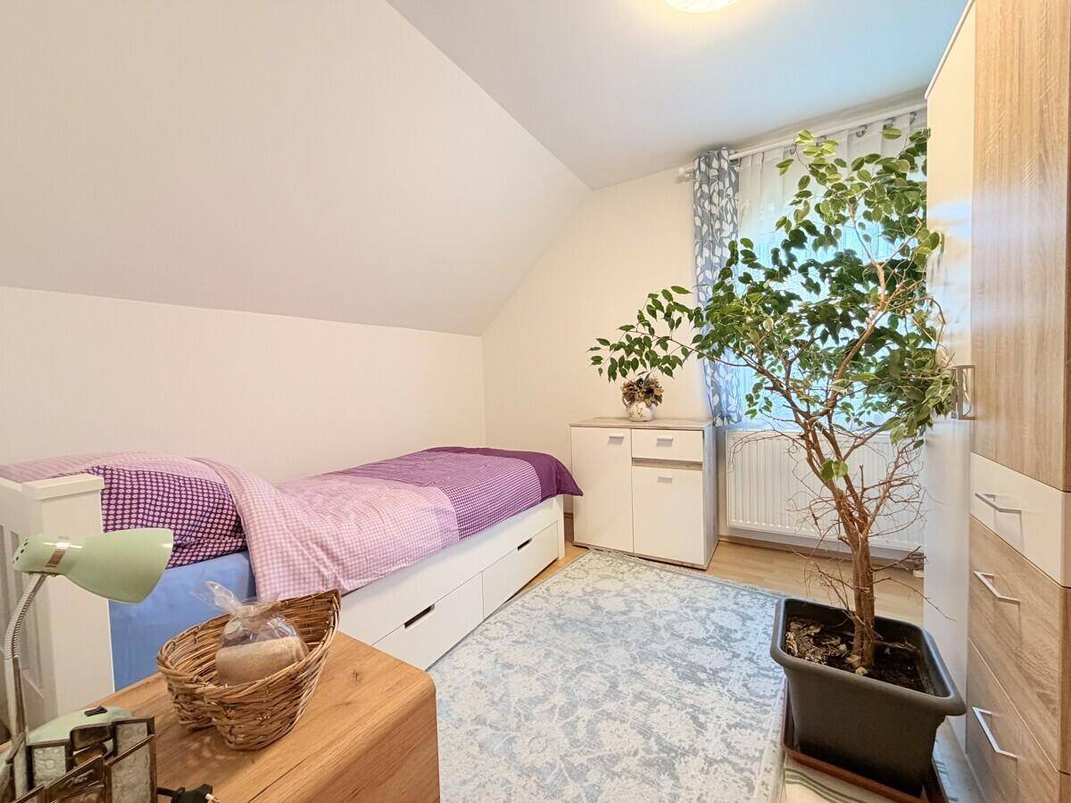 Helles Schlafzimmer im Dachgeschoss mit Einzelbett und großem Fenster.