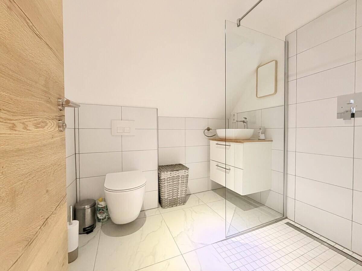 Modernes Badezimmer mit ebenerdiger Dusche, wandhängendem WC und Einzelwaschbecken.