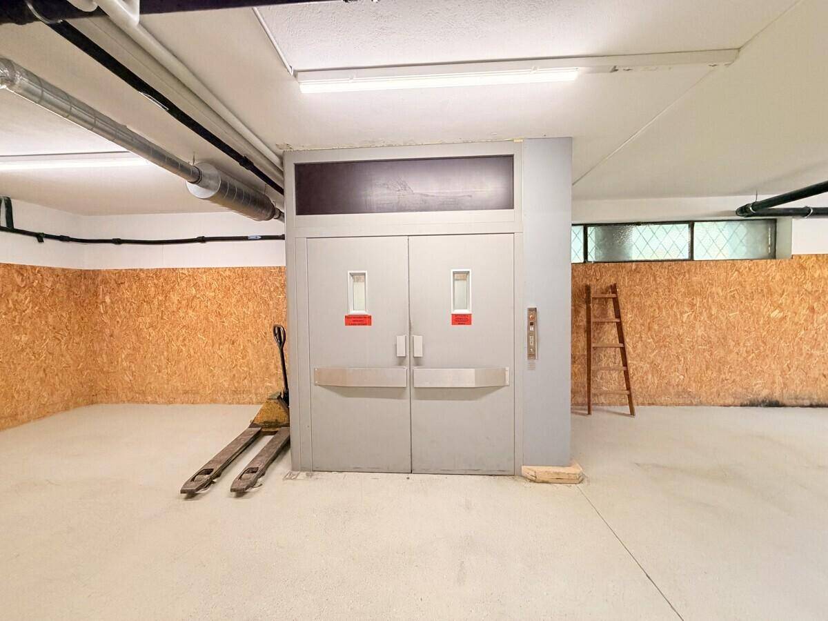 Industriebereich mit einem großen Lastenaufzug, Betonboden und sichtbaren Versorgungsleitungen an der Decke.