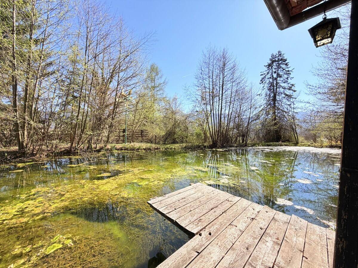 Hölzerner Steg am Teich mit Blick auf das umliegende Grün und das Haupthaus im Hintergrund.