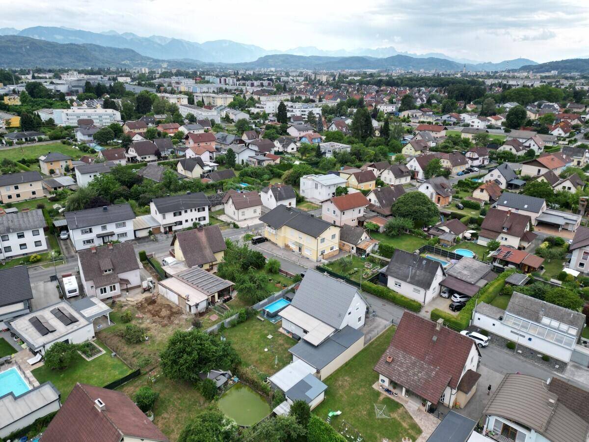 Luftaufnahme einer Wohnsiedlung mit vielen Häusern, Gärten und Bergen im Hintergrund.