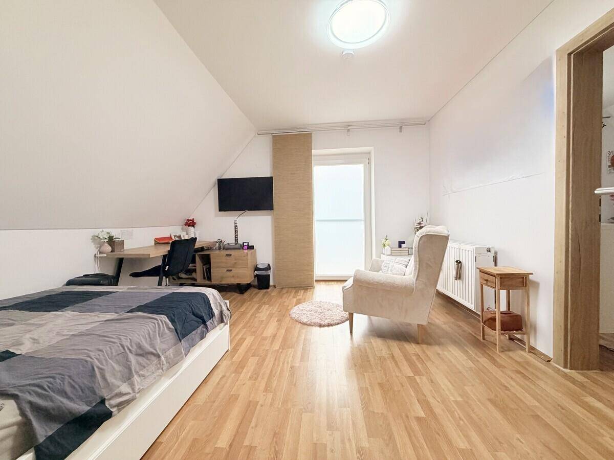 Schlafzimmer im Dachgeschoss mit Bett, Schreibtisch, Laminatboden und Dachschräge.