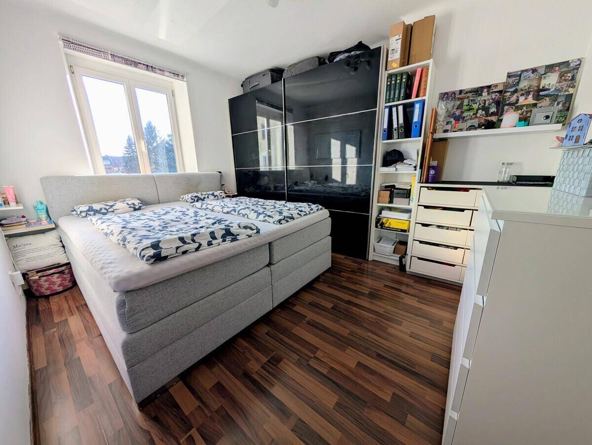 Helles Schlafzimmer mit Doppelbett, dunklem Kleiderschrank und Holzfußboden.