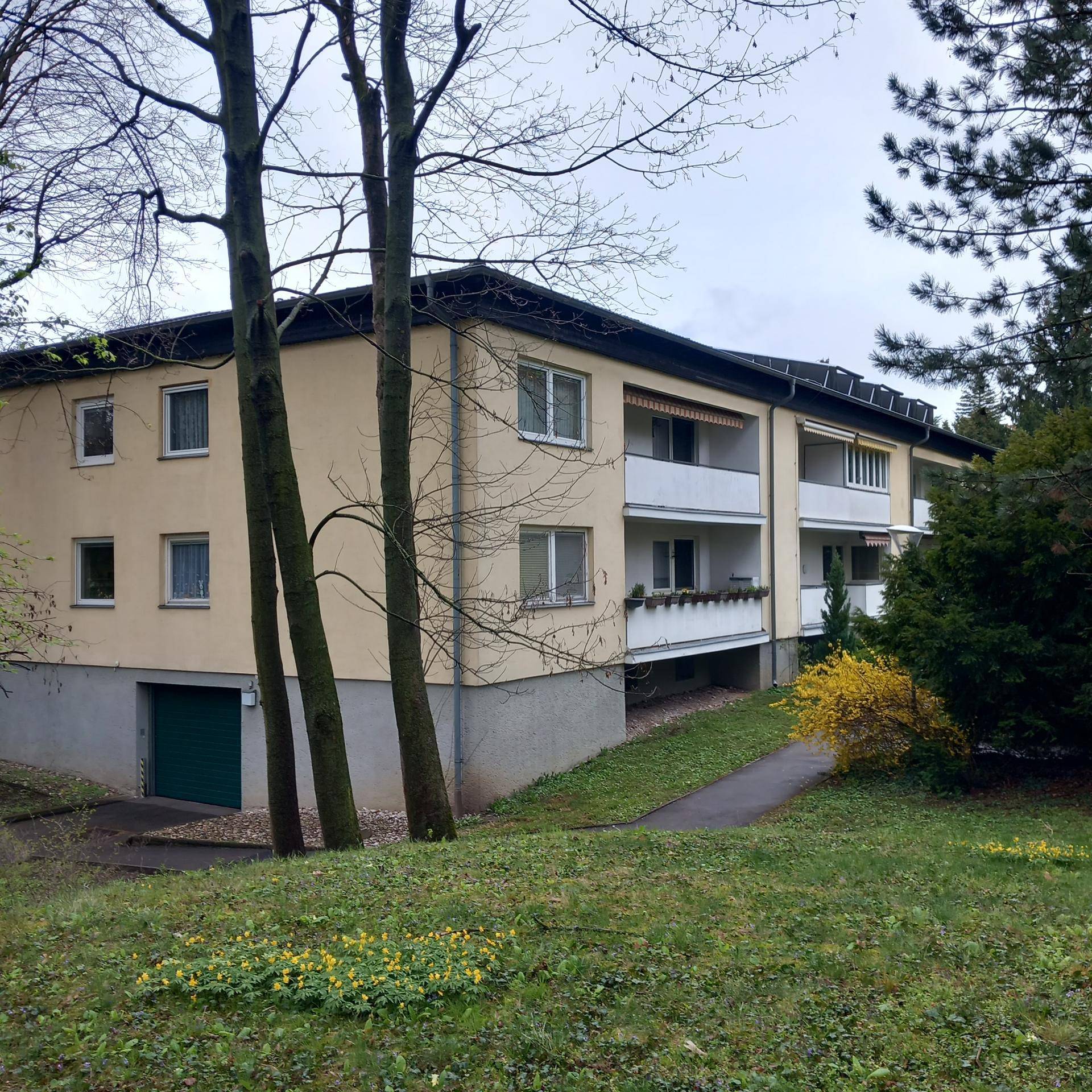 Mehrfamilienhaus mit Balkonen, umgeben von Grünflächen und Bäumen in einer ruhigen Umgebung.