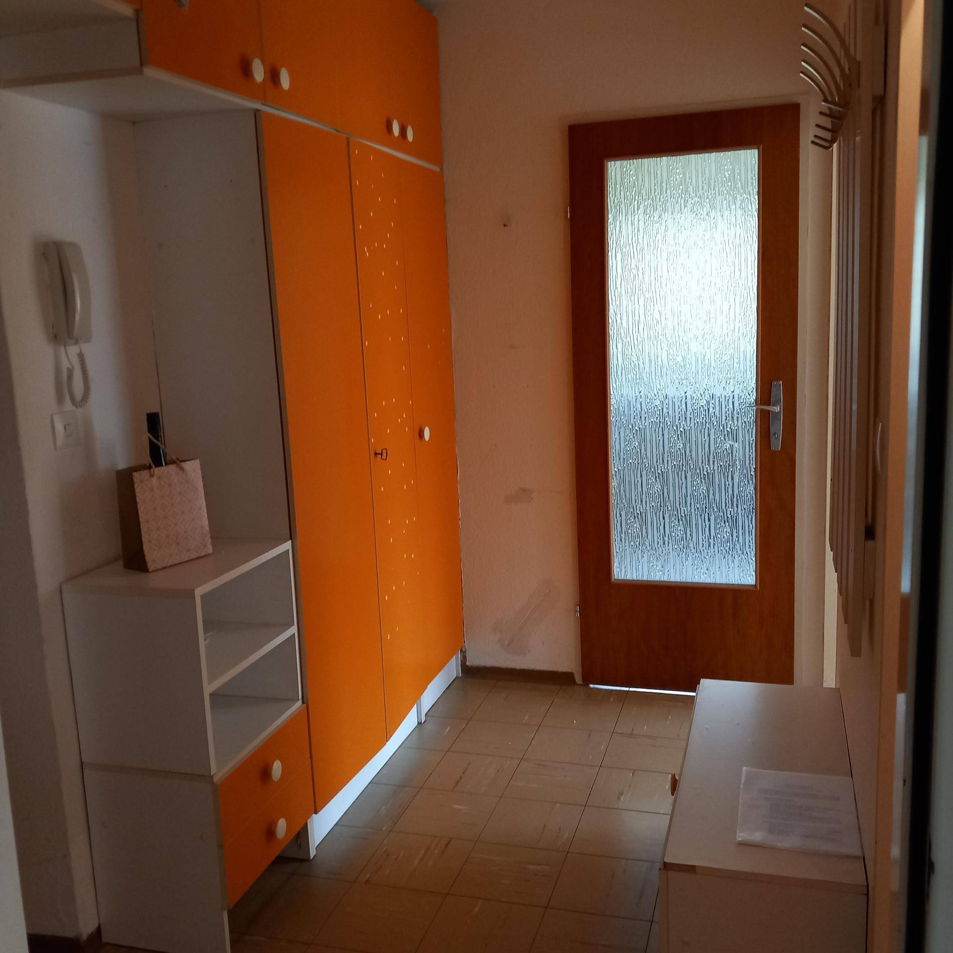 Flur mit farbenfrohen orangefarbenen Schränken, Garderobe und einer Holztür mit Milchglas.