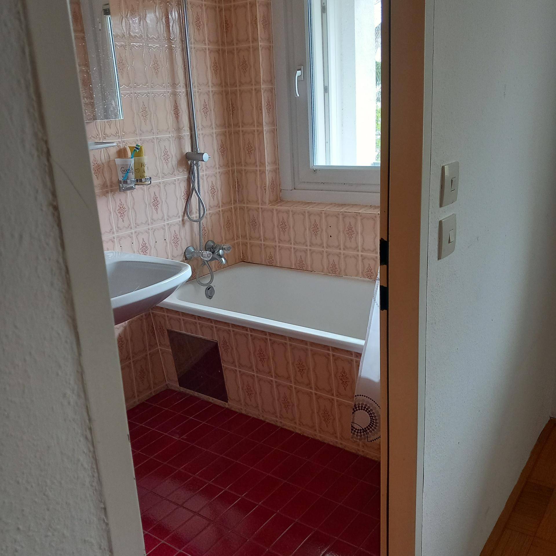 Badezimmer mit Badewanne, Dusche, Waschbecken und Fliesen in Rosa- und Rottönen.