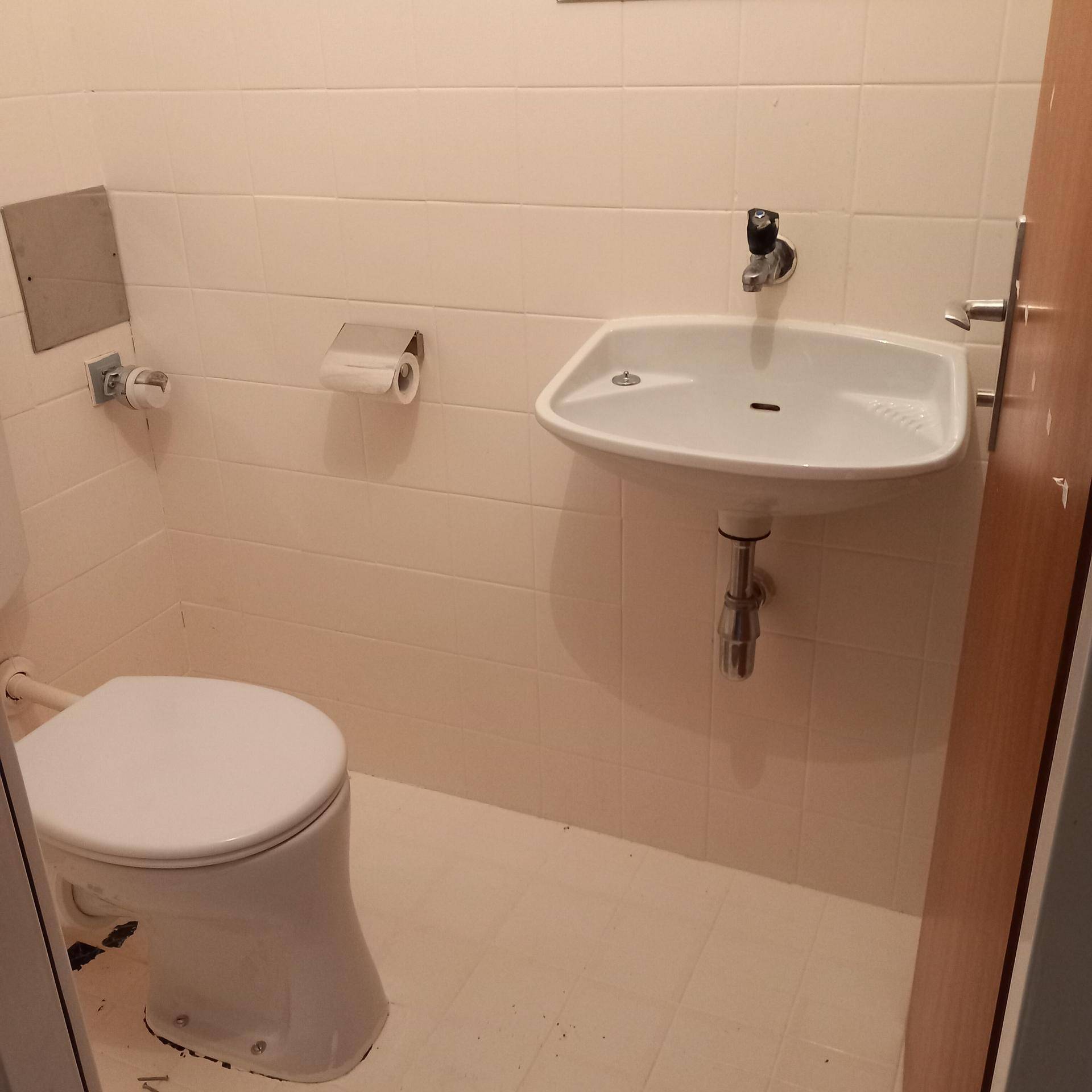Kleines Gäste-WC mit Toilette, Waschbecken und hellbeigen Fliesen an Wänden und Boden.